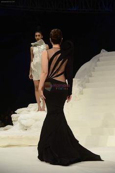 a woman in a black dress walking down the runway