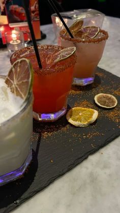 three cocktails are sitting on a tray with lemon slices and garnishes