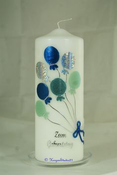 a white candle with blue and green balloons on it