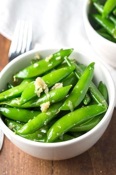 a white bowl filled with green beans on top of a wooden table next to a fork