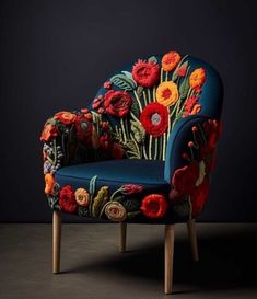 a blue chair with flowers on it in front of a black wall and wooden legs