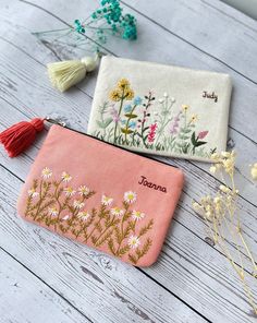 two embroidered pouches with flowers and tassels sitting on a white wooden table