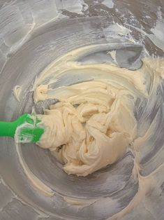 a mixing bowl filled with cream and a green spatula in it's center