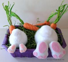 two stuffed animals laying on top of some grass and carrots in a purple container