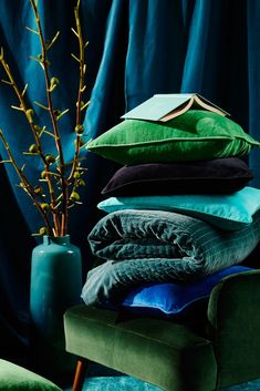 a green chair sitting next to a tall vase filled with flowers and blankets on top of it