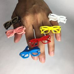 a hand with five pairs of colorful glasses on it's fingers, all in different colors