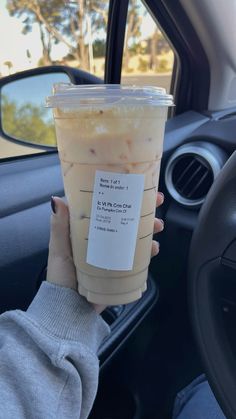 a woman holding up a cup of iced coffee in her hand while sitting in a car