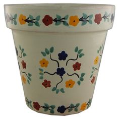 a white flower pot with colorful flowers painted on it's sides and leaves around the rim