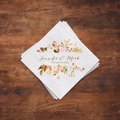 wedding napkins with leaves on them sitting on top of a wooden table