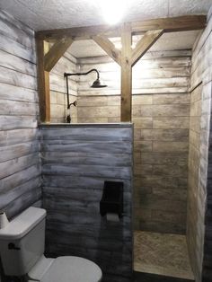 a bathroom with a toilet, shower and wooden paneling on the walls is shown