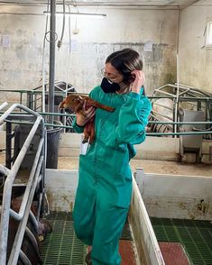 a woman in green coveralls holding a small dog while talking on a cell phone