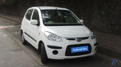 a small white car parked on the side of a road next to a stone wall