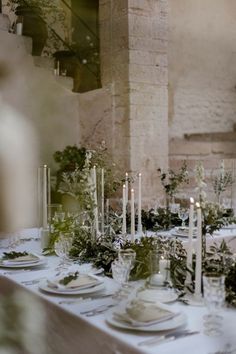 the table is set with candles, plates and greenery for an elegant dinner party