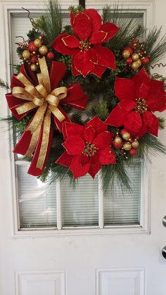 a wreath with poinsettis, pine cones and gold ribbon hanging on a door