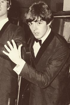 black and white photograph of two men in tuxedos, one holding his arm out