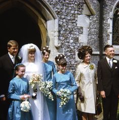 a group of people standing in front of an old building wearing blue dresses and holding bouquets