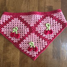 a crocheted dog bandana with cherries on the front and bottom, sitting on a wooden floor