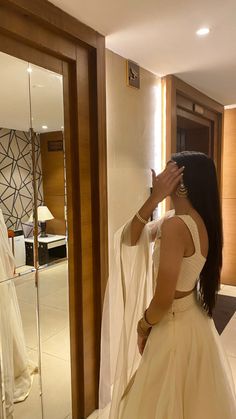 a woman in a wedding dress looking at herself in the mirror and touching her hair