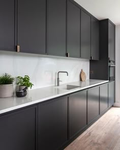 a kitchen with black cabinets and white counter tops, potted plants on the island