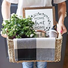 a person holding a basket with some plants in it and a sign that says home sweet home