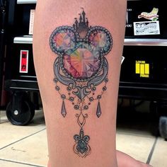 a woman's leg with a disney mouse head tattoo on it and an image of a castle in the background