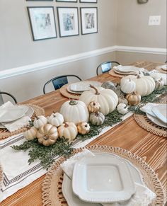 the table is set with white pumpkins and greenery on it, along with plates