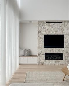 a living room with a large stone fireplace and white drapes on the windowsill