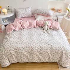 a bed with pink and white comforters, pillows and stuffed animals on the floor