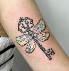 a woman's arm with a dragonfly tattoo on it and a key in the middle