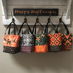 four halloween themed purses hanging from hooks on a wall with happy halloween sign in the background