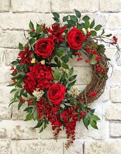 a wreath with red flowers and greenery hanging on a brick wall