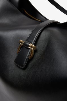 Black leather tote bag from Ferragamo. The large tote bag is made from soft semi-glossy calfskin leather in a softened silhouette, complete with a magnetic golden Gancini clasp that fastens the top strap. Tonal lining and a zipped pocket inside. Measurements: L30 x H13 x W9 cmMade in Italy Luxury Hobo Tote Bag For Business, Calf Leather Tote Shoulder Bag For Business, Sleek Calf Leather Top Handle Shoulder Bag, Sleek Top Handle Calf Leather Shoulder Bag, Classic Business Hobo Bag With Top Carry Handle, Classic Hobo Bag With Top Carry Handle For Business, Sleek Tote Bag With Gold-tone Hardware, Business Bucket Bag With Gold-tone Hardware And Double Handle, Business Bucket Bag With Double Handle And Gold-tone Hardware