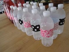 a row of water bottles with pink and black polka dot labels on them sitting on a table