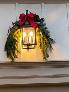 a christmas wreath hanging from the side of a building with two lit candles in it