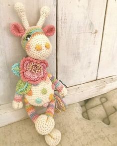 a crocheted stuffed animal with flowers on it's head sitting next to a wooden door