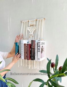 a woman is reaching for some books in front of a wall hanging book rack with an owl on it