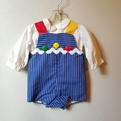 "- This great vintage outfit by C.I. Castro and Co. is perfect for any occasion. The romper is blue and white striped with one red strap and one yellow strap. It is fully lined and buttons at back and snaps between legs. The front is detailed with a giant white rick rack trim and 3 plastic fish buttons. The back has large red buttons. The shirt underneath is white and long sleeved with buttons down back. Size is: 12 months Length: 15\"	in stock	34.65 USD	"	3.50 USD	Clothing > Boys' Clothing > Ba Fitted Cotton Overalls With Buttons, Playful Fitted Blue Jumpsuits And Rompers, Long Sleeve Cotton Overalls With Buttons, Cotton Overalls With Sleeves And Buttons, Vintage Blue Cotton Overalls, Fitted Cotton Jumpsuits And Rompers For Playtime, Blue Overalls With Buttons, Playful Blue Cotton Overalls, Retro Blue Cotton Overalls