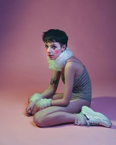 a woman sitting on the ground with her legs crossed and wearing white gloves over her body