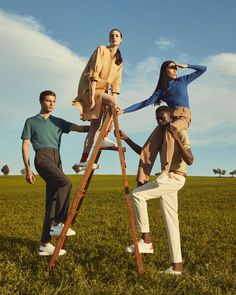 three people standing on top of a ladder in the middle of a field with grass