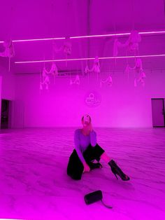 a woman sitting on the floor in front of a purple light with her legs crossed