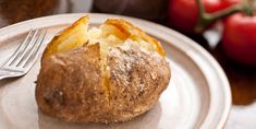 a baked potato on a white plate with a fork and tomatoes in the back ground