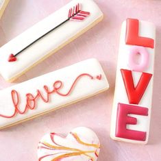 three decorated cookies sitting on top of a pink surface with the word love spelled out