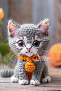 a small crocheted kitten wearing a yellow tie and sitting on top of a wooden table