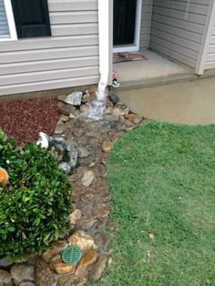 a small garden with rocks and water coming out of the hole in the ground, next to a house