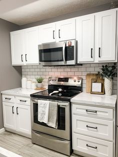 a kitchen with white cabinets and stainless steel stove top oven in the middle of it