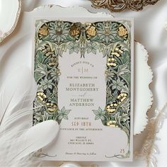 an ornate wedding card with gold and green details on it, surrounded by white feathers