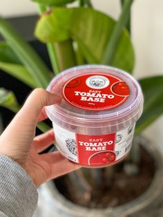 a person holding up a container of yogurt next to a potted plant