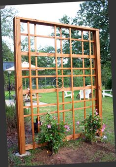 a wooden trellis with flowers growing in the ground next to it and a cat