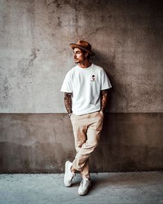 a man leaning against a wall wearing a hat