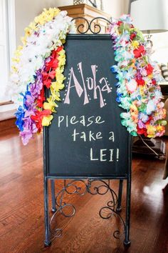 a chalkboard sign decorated with colorful leis and saying aloha please take a lei